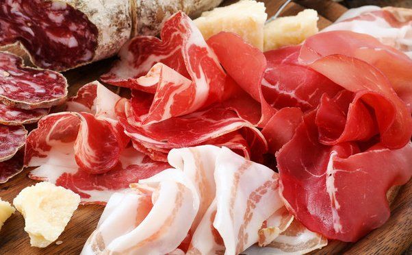 Sliced cured meats and bacon on a wooden board