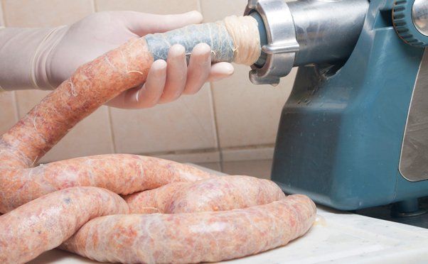 Hands guiding fresh sausage into casing on a sausage stuffer